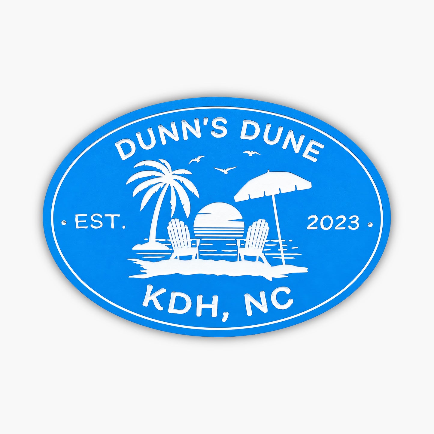 The Personalized Oval Beach House Sign is blue and white, featuring a tropical scene with a palm tree, two beach chairs, an umbrella, and a sunset over water. It reads Dunns Dune, Est. 2023, KDH, NC, making it ideal for your vacation rental sign!.