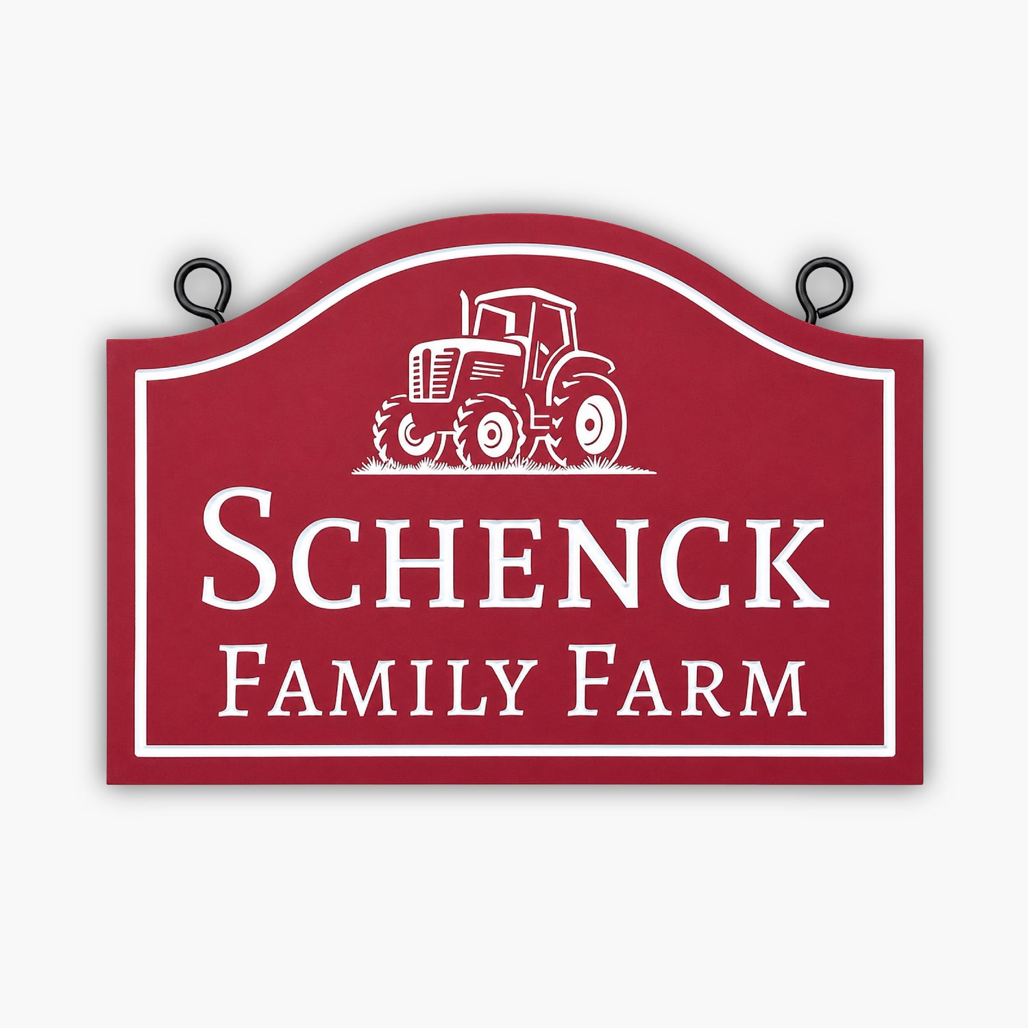 A red sign with white trim shows an illustration of a tractor above the words Schenck Family Farm. The sign is propped outdoors against tan siding.