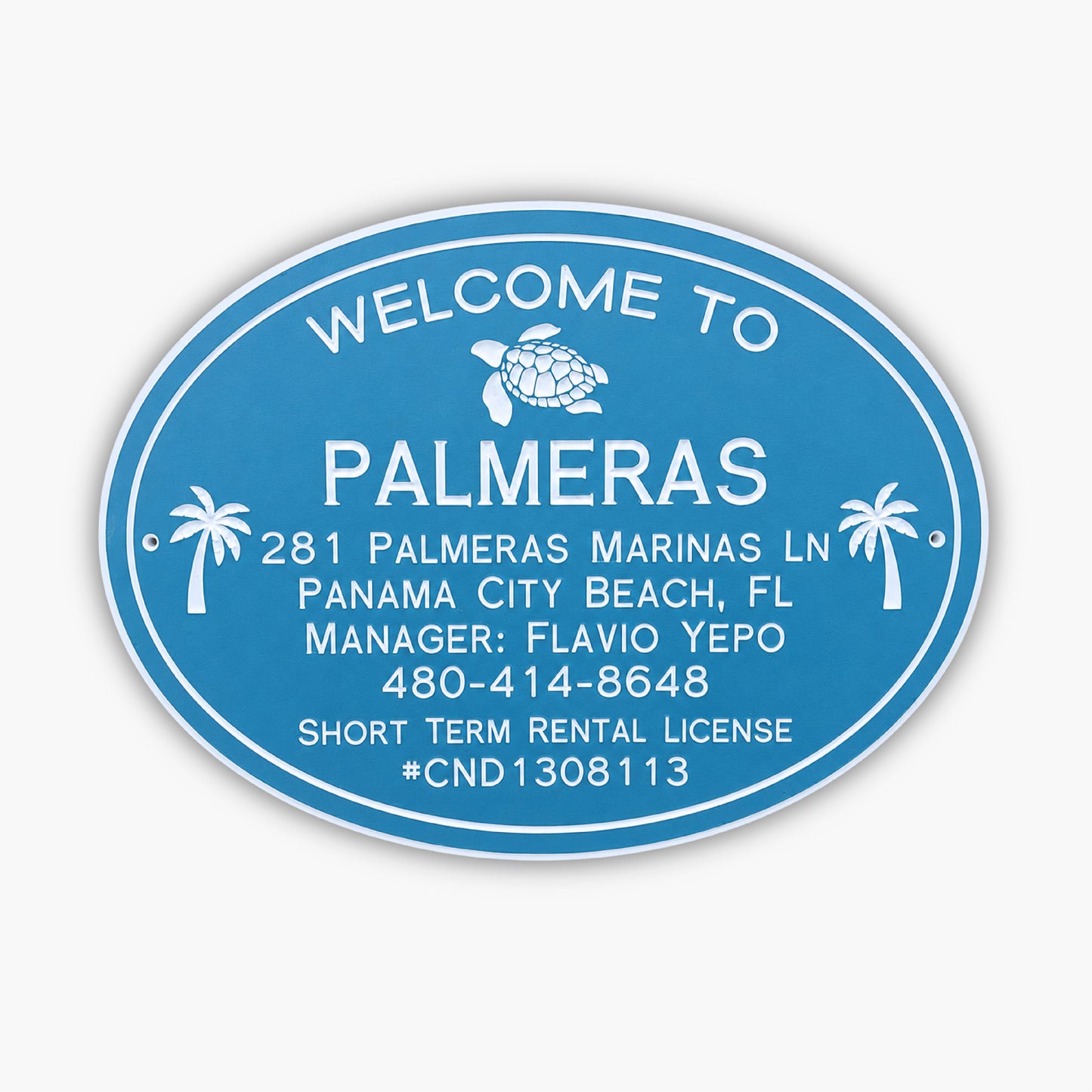 A blue oval sign with white text reads: Welcome to Palmeras. Below are an address, contact details, and a license number: 281 Palmeras Marinas Ln, Panama City Beach, FL, Manager: Flavio Yepo, 480-414-8648, Short Term Rental License #CND1308113.