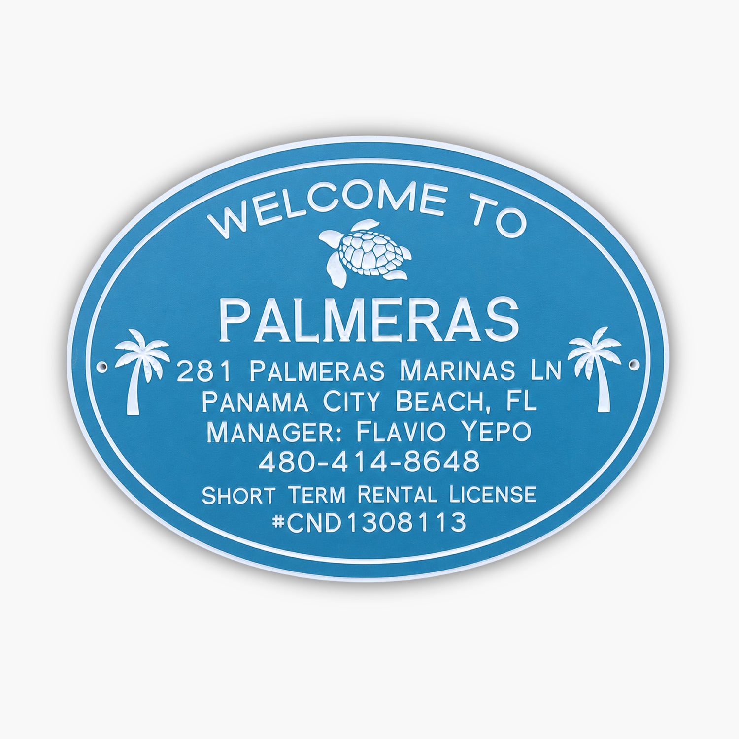 A blue oval sign with white text reads: Welcome to Palmeras. Below are an address, contact details, and a license number: 281 Palmeras Marinas Ln, Panama City Beach, FL, Manager: Flavio Yepo, 480-414-8648, Short Term Rental License #CND1308113.