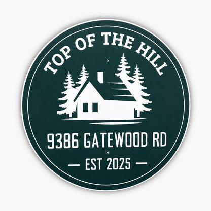 Round green sign with white design and text: TOP OF THE HILL at the top, featuring a house silhouette with trees. Below, text reads 9386 GATEWOOD RD and EST 2025. Set against a light-colored siding background.