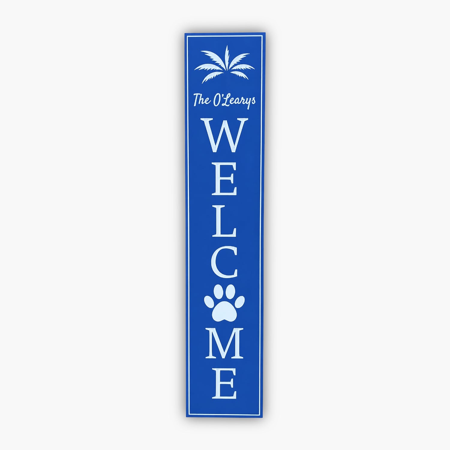 A blue welcome sign with a palm tree graphic at the top, text The OLearys, and the word WELCOME written vertically with a paw print replacing the letter O. The sign leans against tan siding.