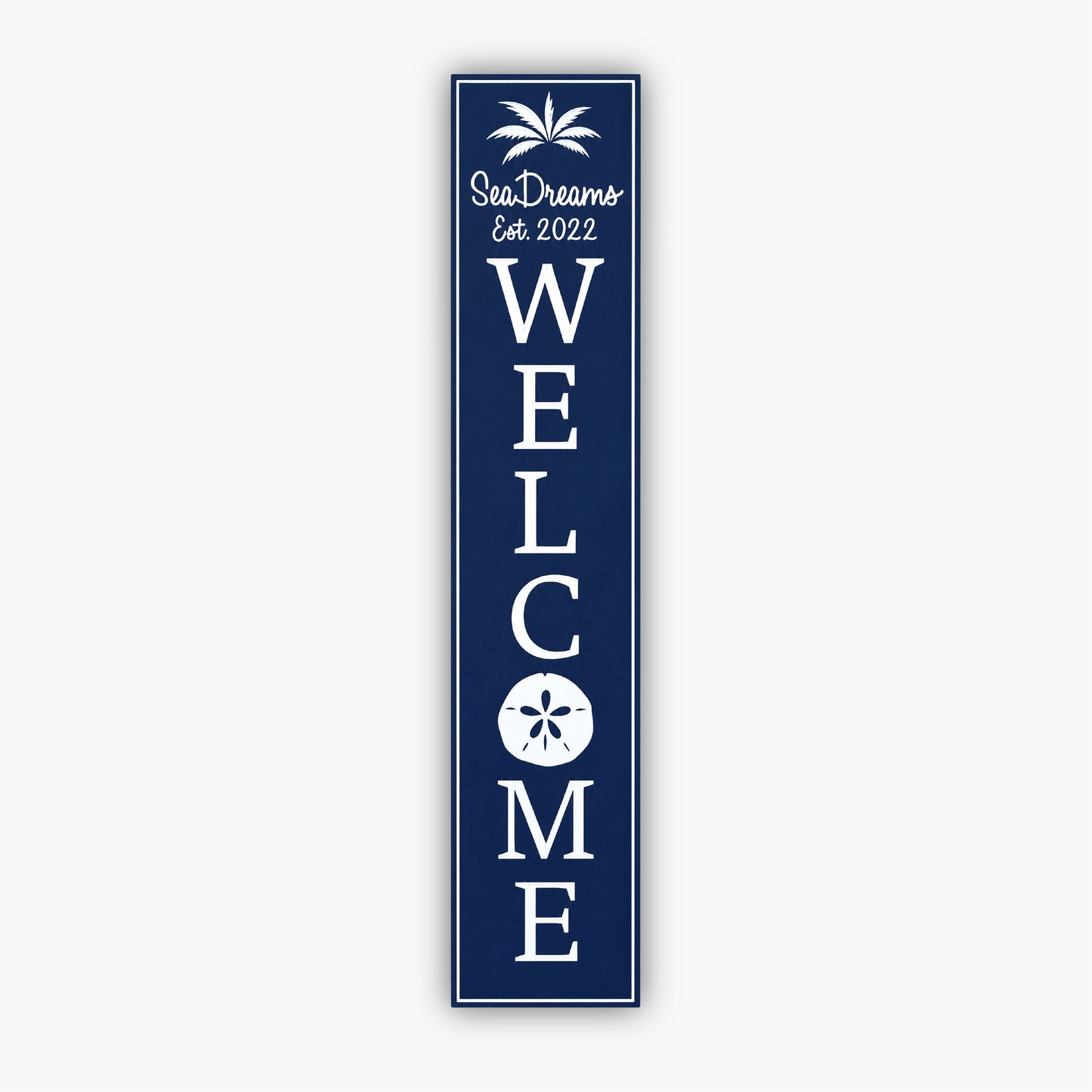 Tall blue vertical welcome sign with white text reading Sea Dream and Est. 2022 at the top, with a palm tree graphic. Large vertical WELCOME text follows, featuring a sand dollar graphic within the O. The background is a beige siding wall.
