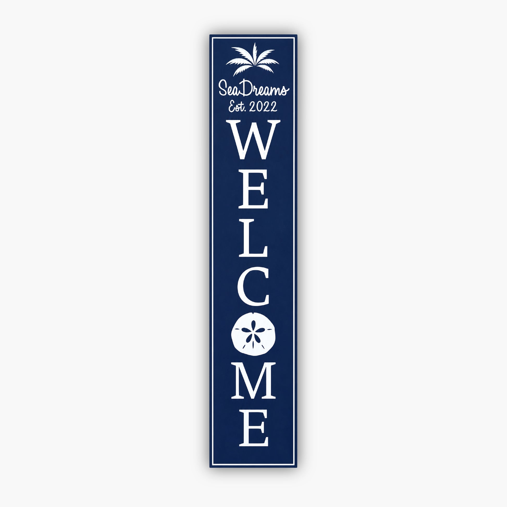 Tall blue vertical welcome sign with white text reading Sea Dream and Est. 2022 at the top, with a palm tree graphic. Large vertical WELCOME text follows, featuring a sand dollar graphic within the O. The background is a beige siding wall.
