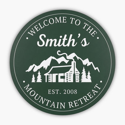 The Custom Carved Round PVC Cabin Sign welcomes guests with Welcome to the Smiths Mountain Retreat and Est. 2008, featuring a white illustration of a cabin, trees, and mountains, capturing the serene essence of this retreat beautifully.