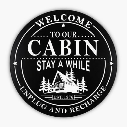 Custom Carved Round PVC Cabin Sign featuring a black circular design with Welcome to Our Cabin, Stay A While, Unplug and Recharge around an illustration of an A-frame cabin among trees. Established 1976 is displayed at the bottom.