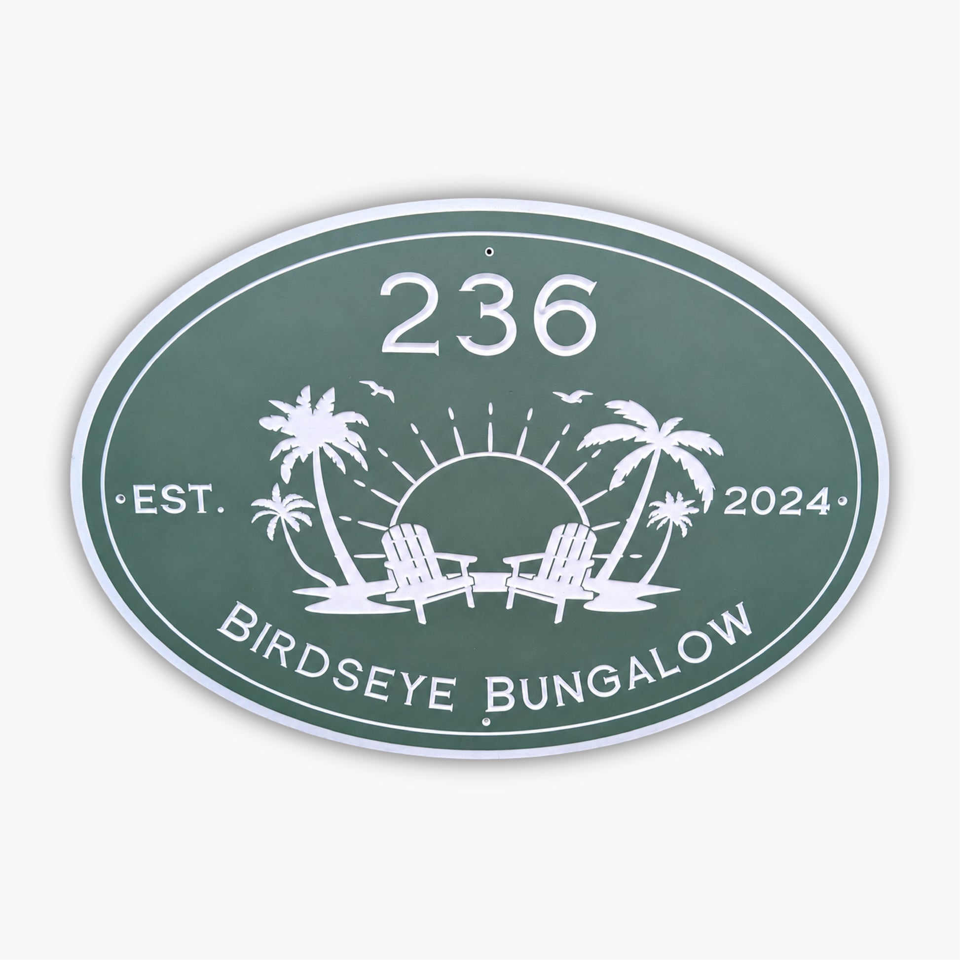 The Personalized Oval Custom Beach House Sign is green with white text, displaying 236 Birdseye Bungalow and Est. 2024. It features a sun setting behind two palm trees and lounge chairs, surrounded by birds.