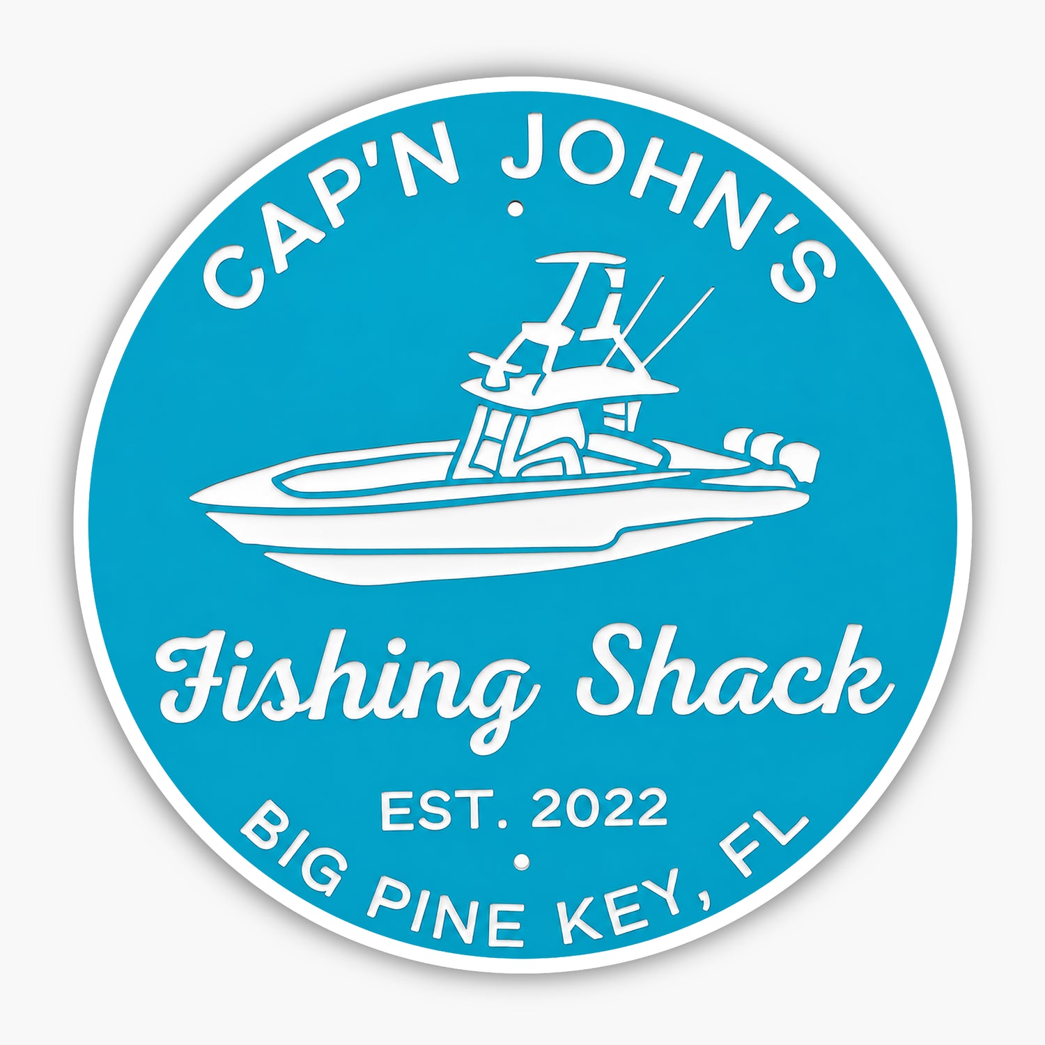The Personalized Custom Round Beach House Sign Coastal Decor is a blue PVC sign with a white boat illustration, reading Capn Johns Fishing Shack, Est. 2022, Big Pine Key, FL. It is durable and mounted on a gray wall.