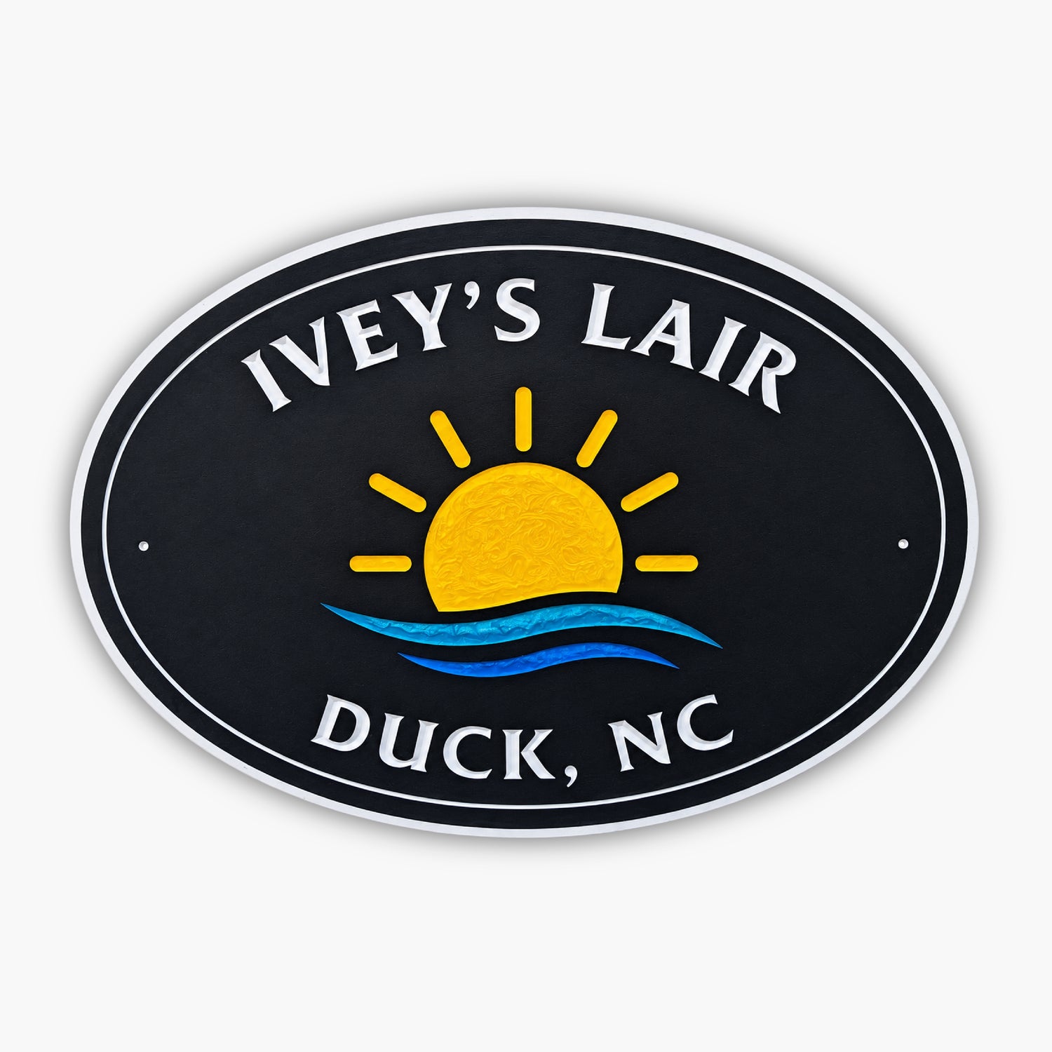 A black oval sign with a vibrant yellow sun and blue waves design. The text reads Iveys Lair at the top and Duck, NC at the bottom, evoking the charm of an art gallery by the sea.