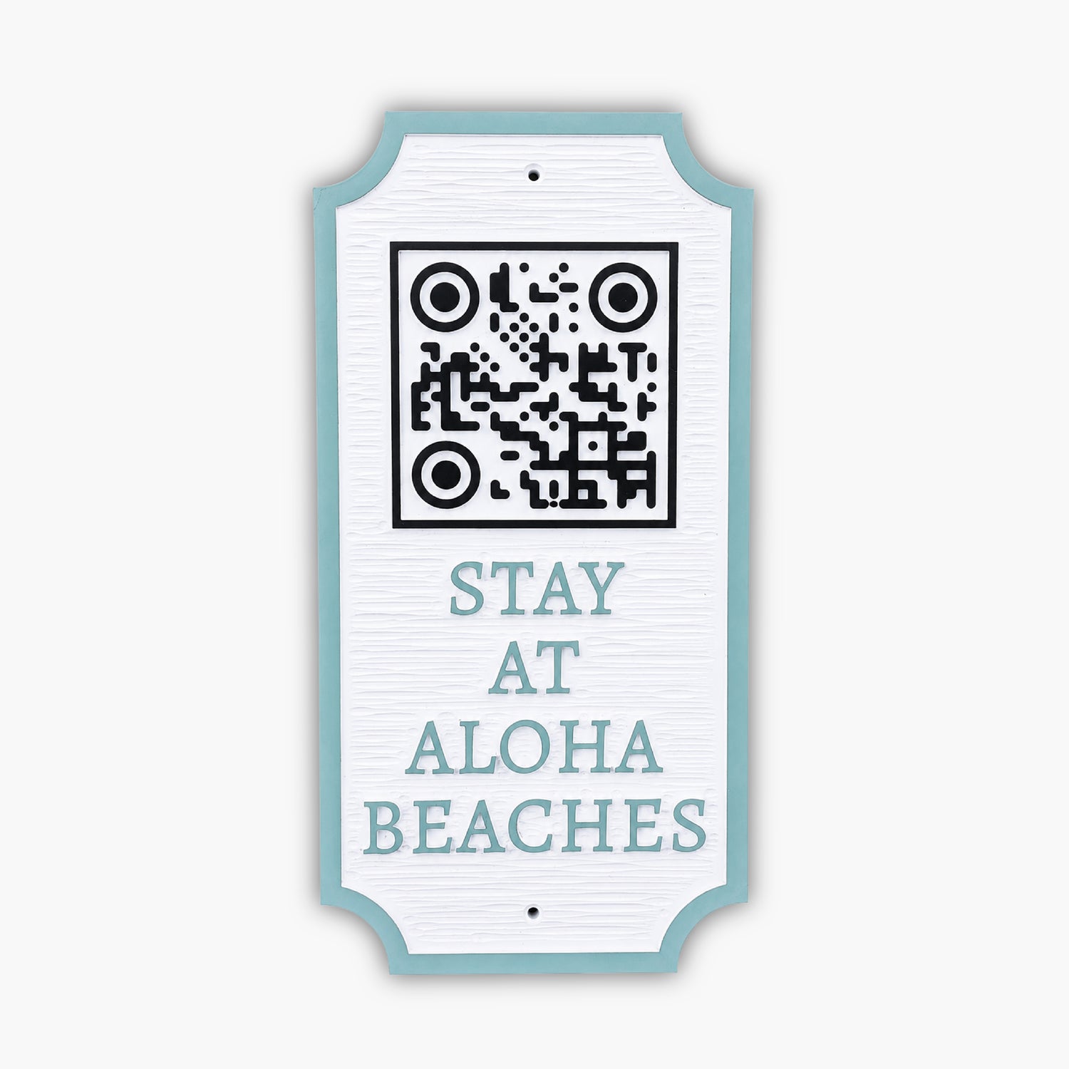 A decorative sign with a QR code at the top and the words STAY AT ALOHA BEACHES below, leaning against a beige paneled wall.