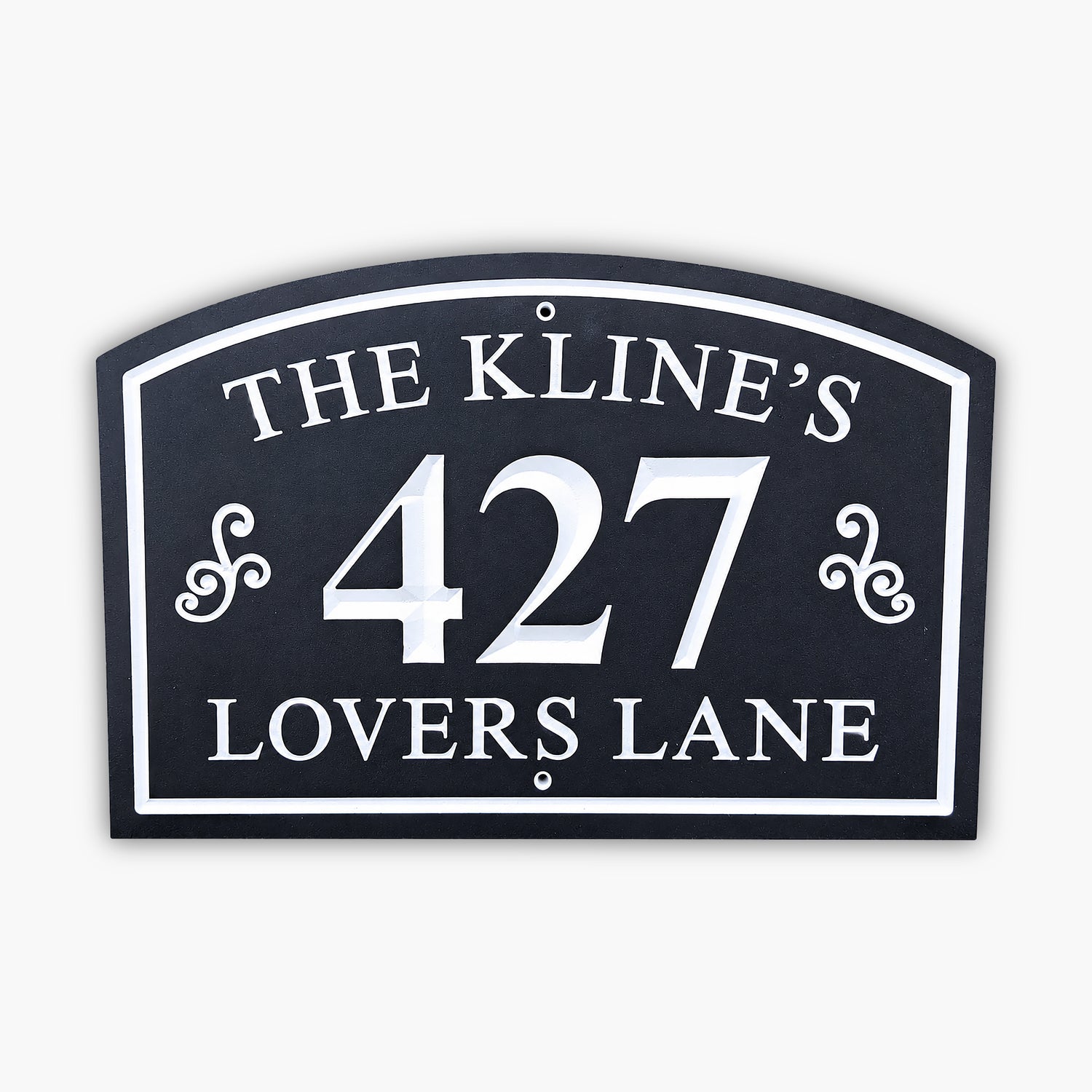 A black and white house sign reads THE KLINES 427 LOVERS LANE in bold letters and numbers, with decorative flourishes on each side of the number. The sign is mounted on a light-colored wall.