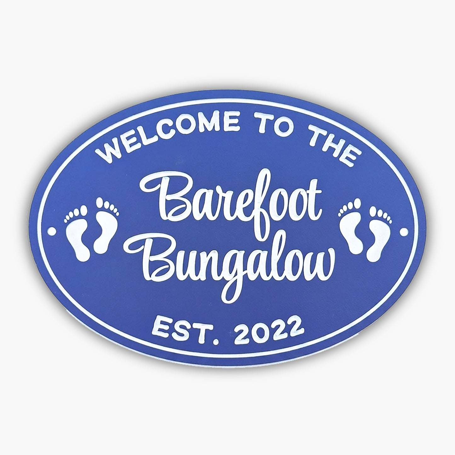 Blue oval sign with white text reading Welcome to the Barefoot Bungalow surrounded by footprint graphics, inviting guests into a relaxing retreat. Est. 2022 is written at the bottom, adding a touch of charm akin to an art gallerys timeless appeal.