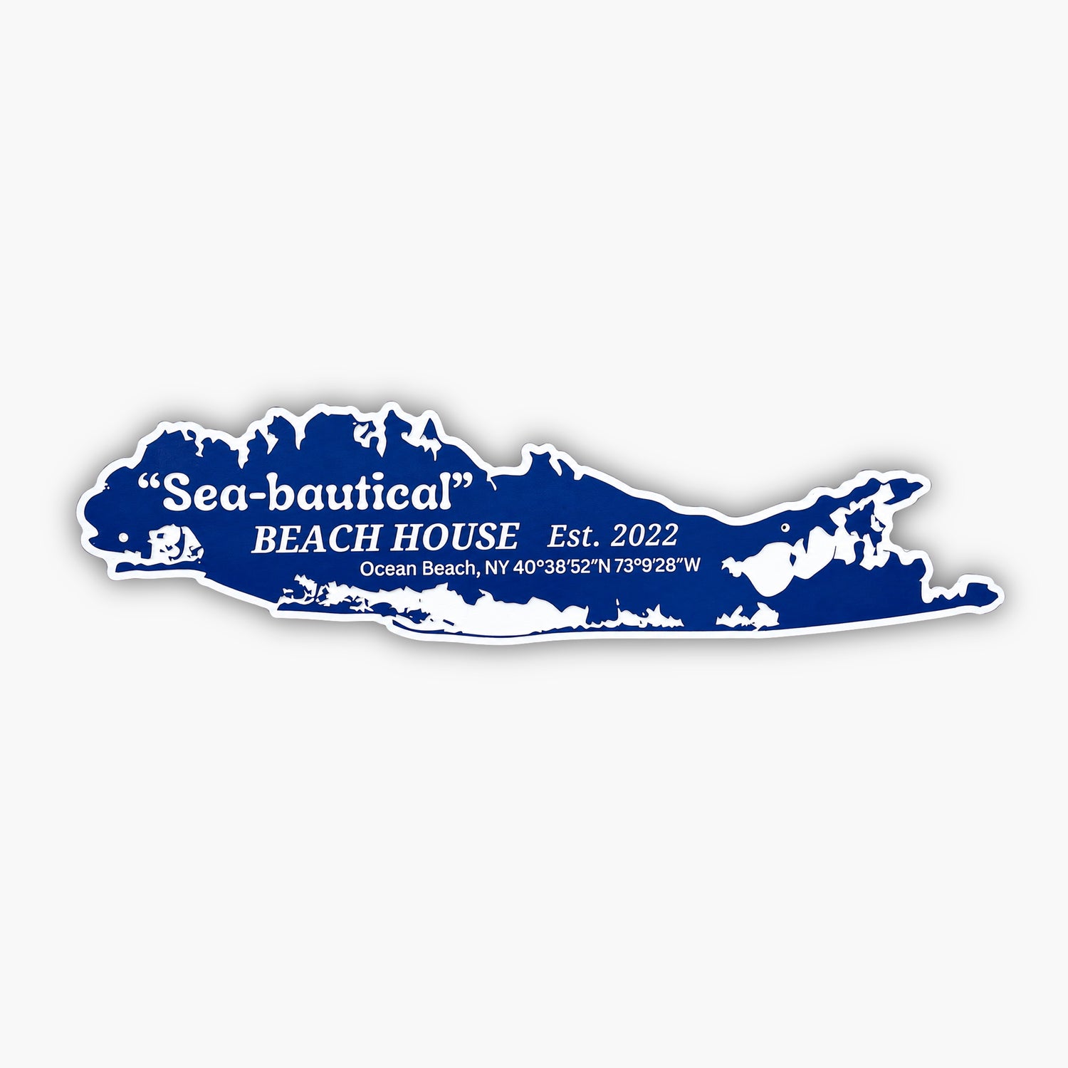 A Long Island-shaped sign in blue and white reads Sea-bautical Beach House Est. 2022 Ocean Beach, NY 40°3852N 73°928W. This Custom Sign for Homes & Rentals is placed on a textured brown surface with a beige background.