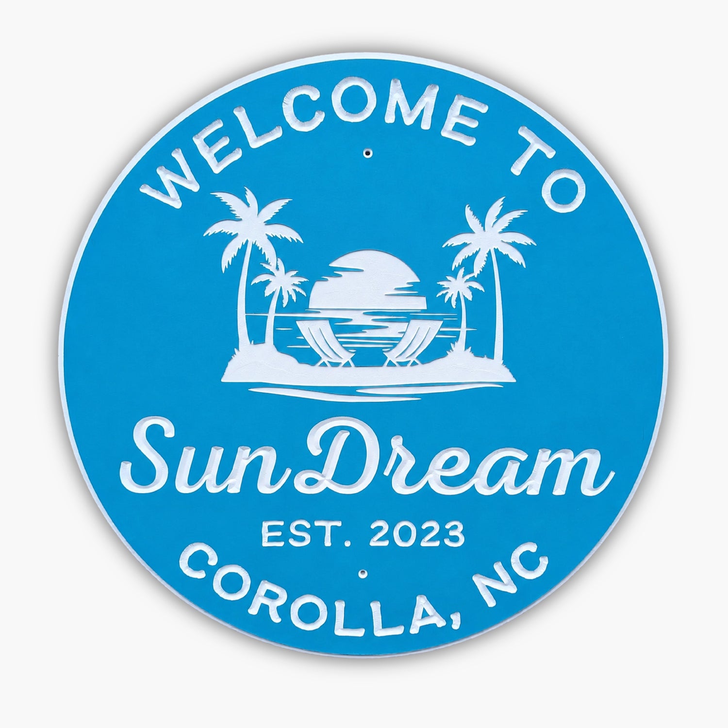 The Personalized Custom Round Beach House Sign Coastal Decor is blue with white text: Welcome to SunDream, Est. 2023, Corolla, NC. It features a beach scene with palm trees, a sunset, and two lounge chairs.