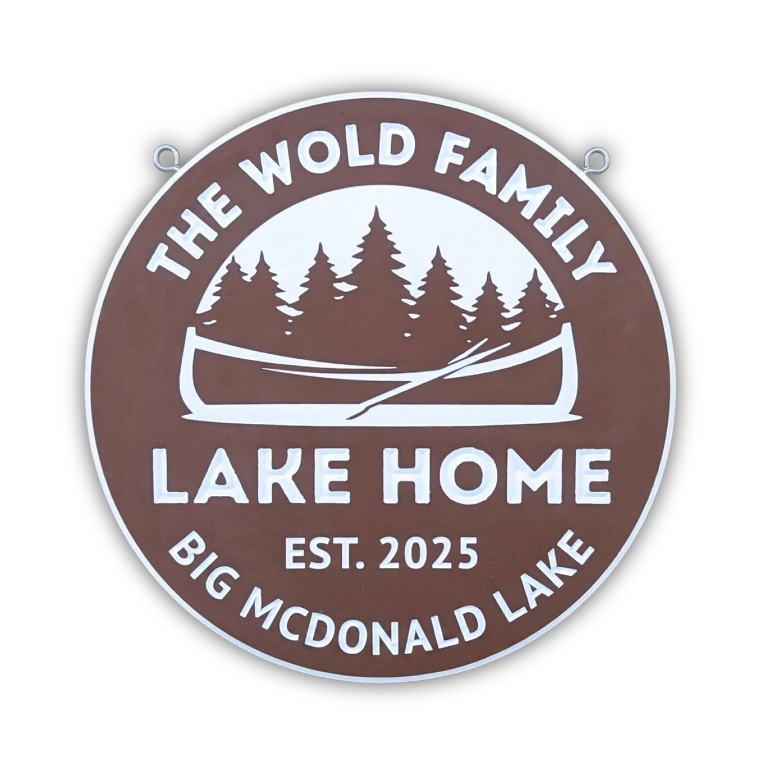 A round brown sign with white text reads The Wold Family Lake Home, Est. 2025, Big McDonald Lake. The sign features a canoe and pine trees in the center.