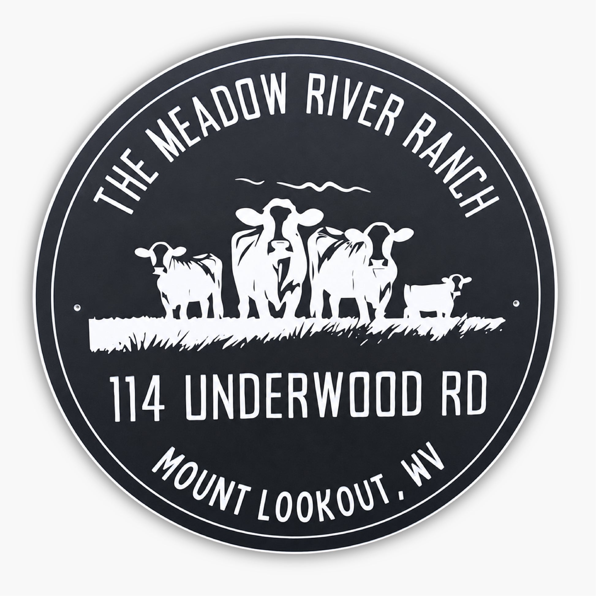 A round sign with The Meadow River Ranch at the top, 114 Underwood Rd, and Mount Lookout, WV at the bottom. In the center, there are silhouettes of three cows and a small calf standing on grass. The sign has a black background with white text and images.