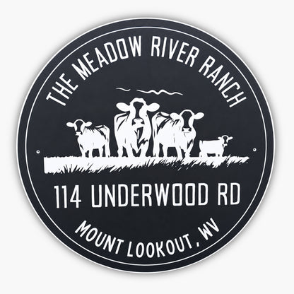A round sign with The Meadow River Ranch at the top, 114 Underwood Rd, and Mount Lookout, WV at the bottom. In the center, there are silhouettes of three cows and a small calf standing on grass. The sign has a black background with white text and images.
