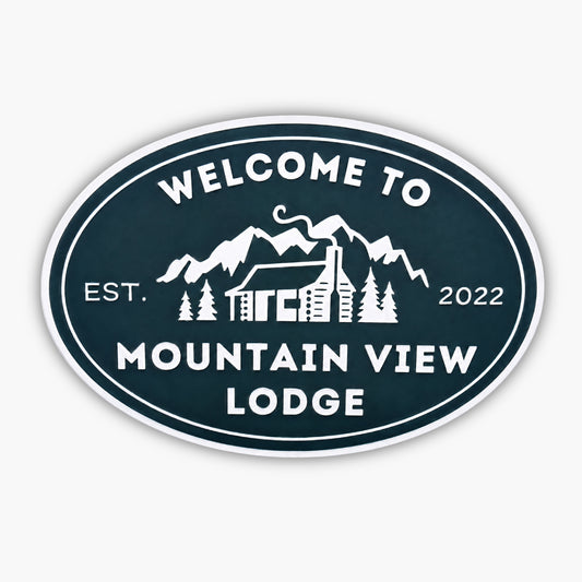 Oval sign reads Welcome to Mountain View Lodge in white, featuring a cabin with a chimney among trees and mountains, echoing the charm of Personalized Oval Custom Beach House Signs Coastal Decor. Established in 2022.