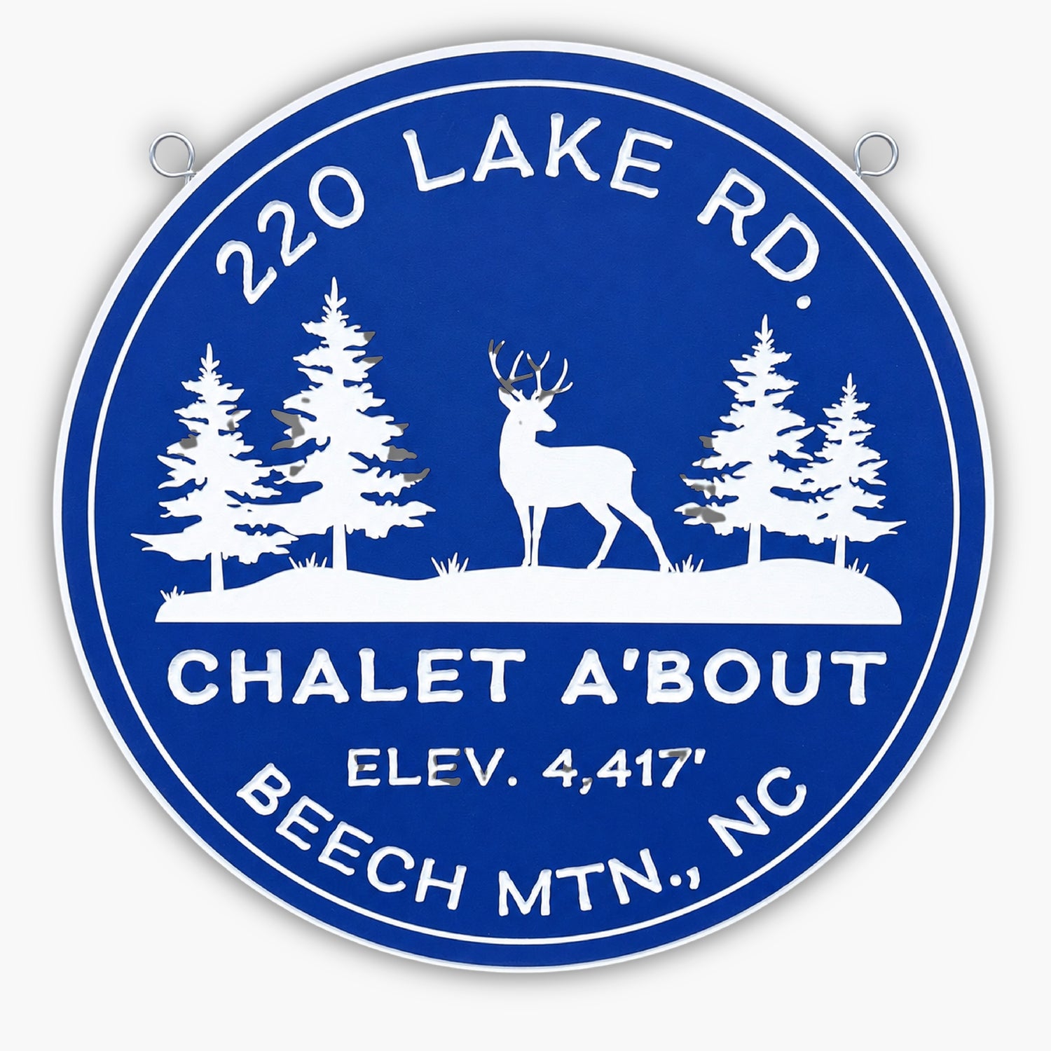 A circular blue pvc sign with white text and silhouettes of a deer and three trees exudes rustic charm. Reading 220 Lake Rd., Chalet A'Bout, Elev. 4,417, Beech Mtn., NC, its perfect for any nature lovers gallery. Two small metal loops at the top make it easy to hang.