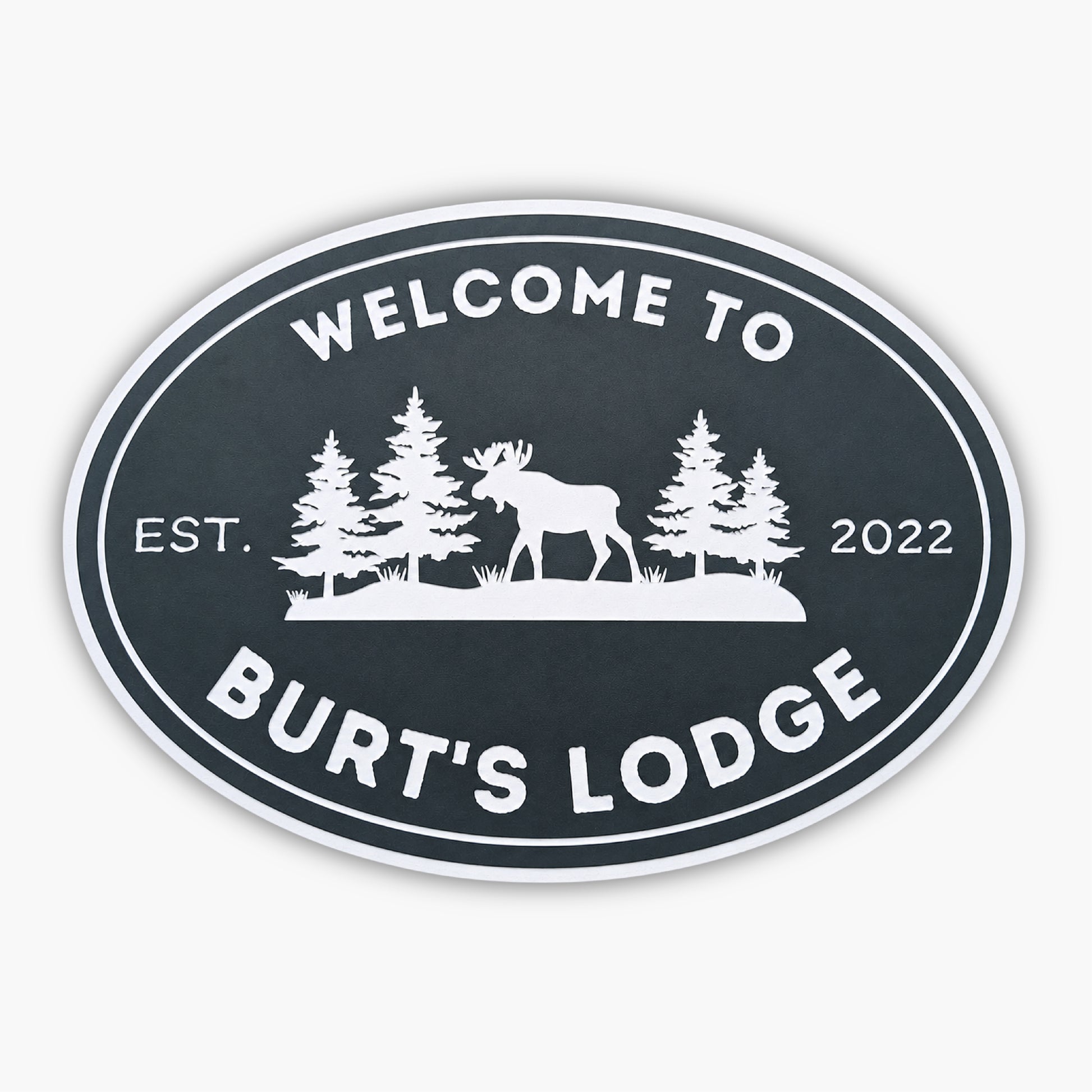 The Personalized Oval Custom Beach House Sign features Welcome to Burts Lodge, showcasing a moose and pine trees silhouette. Its dark background with white lettering reads Est. 2022, echoing the elegance of classic coastal decor.