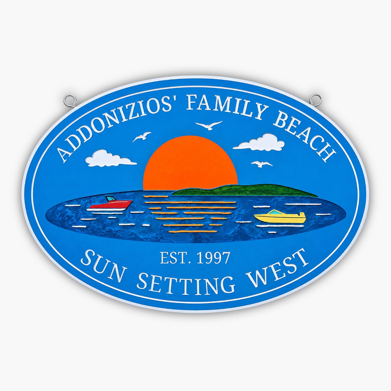 A blue oval sign reads Addonzios Family Beach - Sun Setting West - Est. 1997. Its like a gallery image, featuring a vivid sunset over water with two boats, a small island, and seagulls soaring above.
