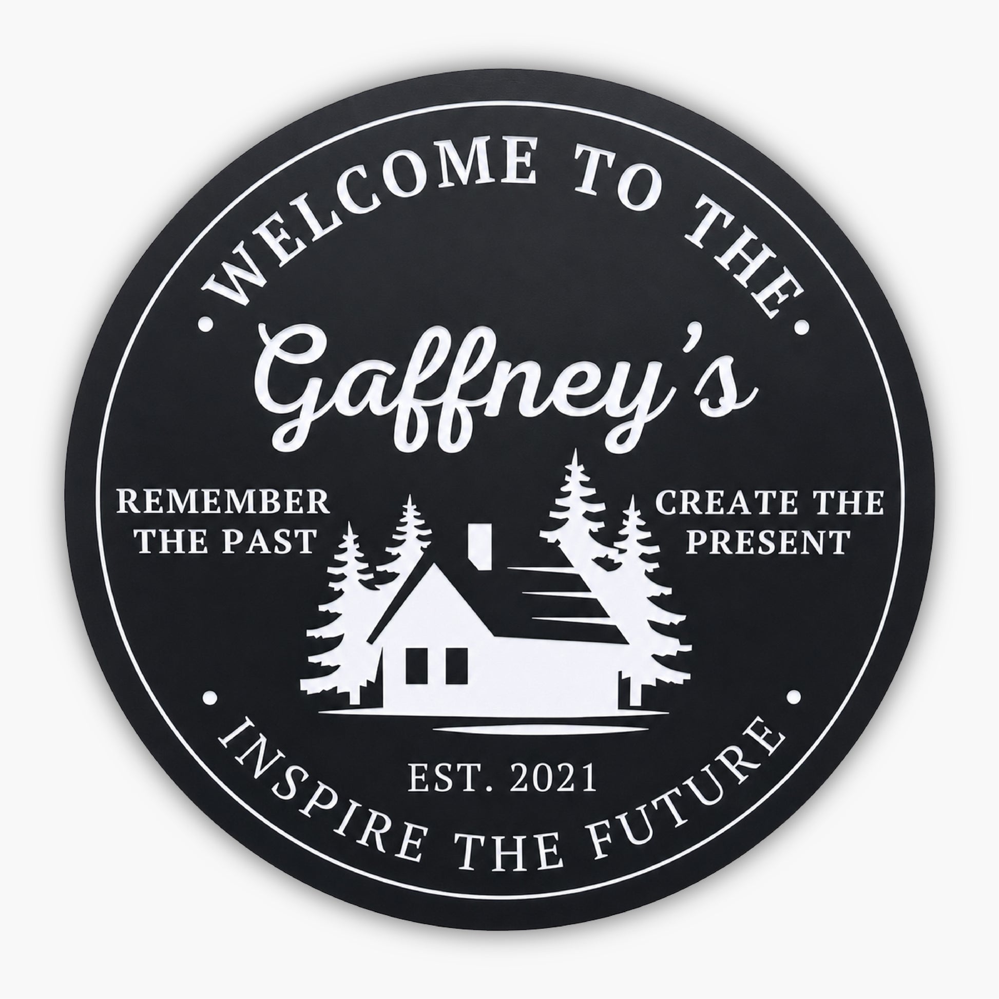 The Personalized Round Cabin Sign features a black circular background with white text: Welcome to the Gaffneys at the top. A custom cabin silhouette and trees grace the center, flanked by Remember the Past, Create the Present. Below is Est. 2021, with Inspire the Future at the bottom.