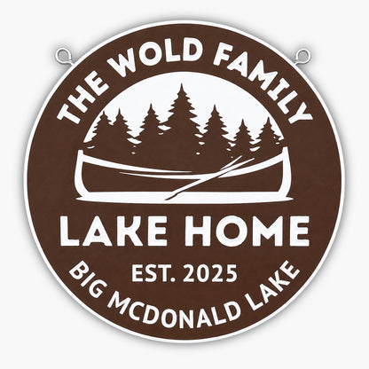 A round brown sign with white text reads The Wold Family Lake Home, Est. 2025, Big McDonald Lake. The sign features a canoe and pine trees in the center.