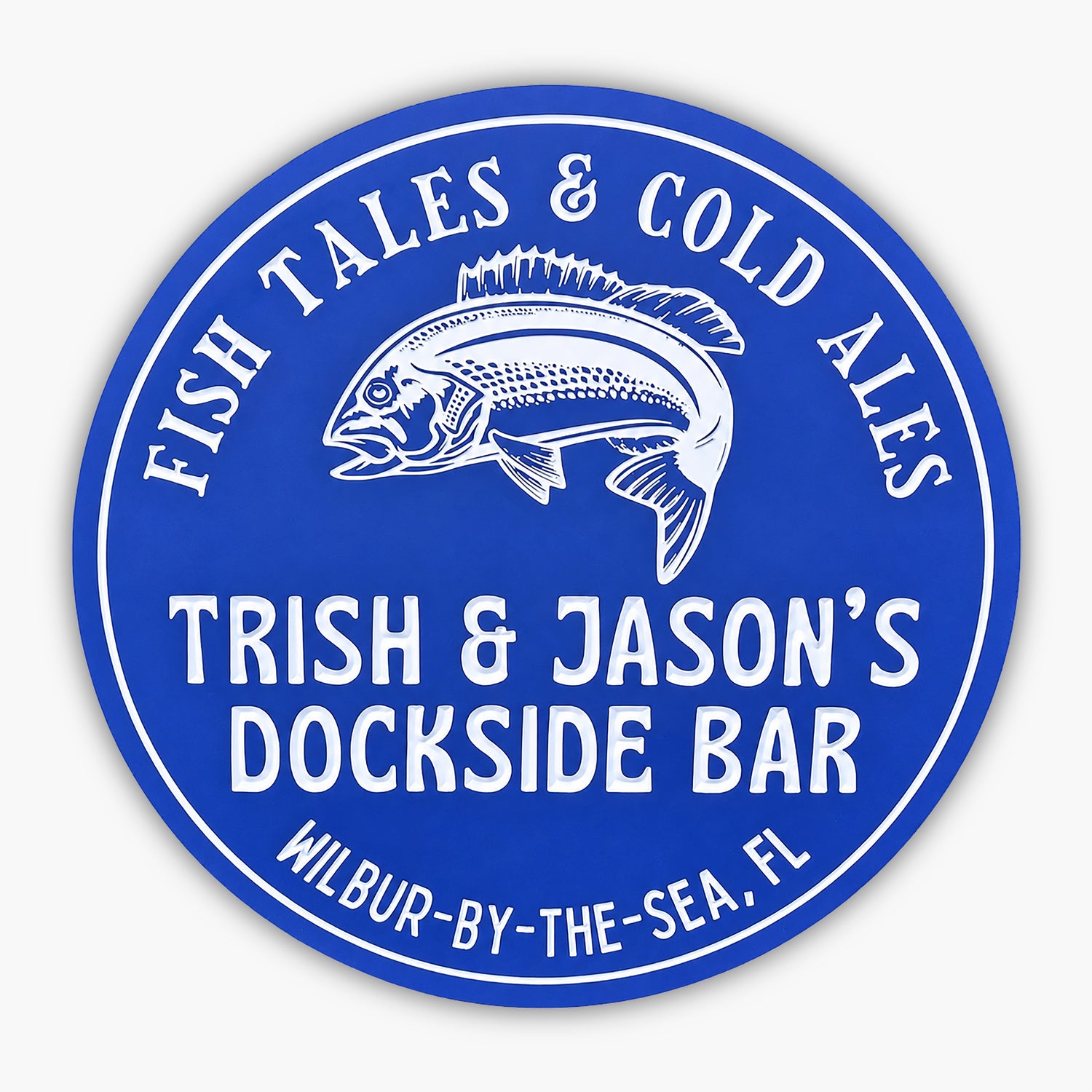 A blue circular sign with a fish illustration, reading: “Fish Tales & Cold Ales, Trish & Jason’s Dockside Bar, Wilbur-by-the-Sea, FL,” displayed against beige siding.